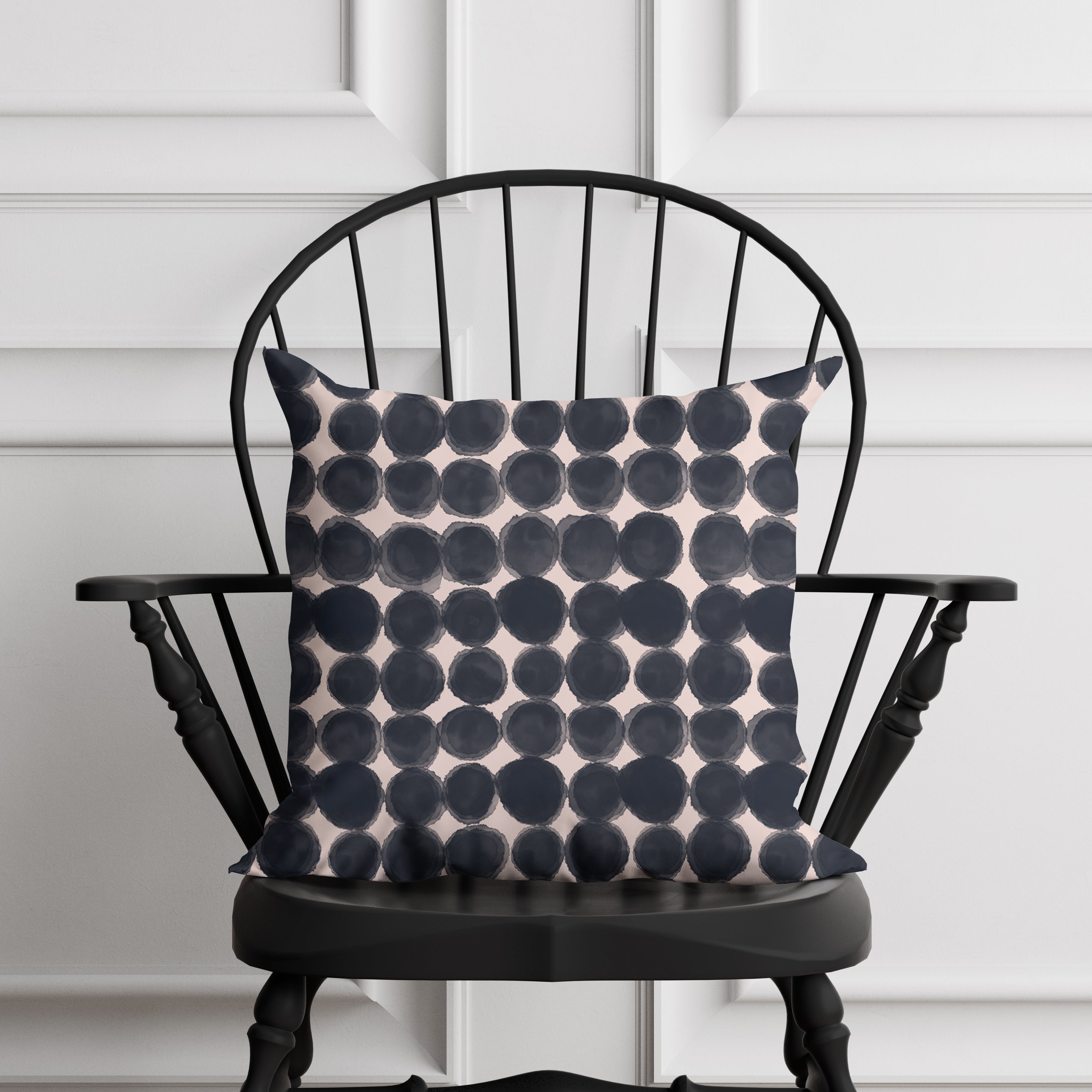 Black and pink patterned pillow on a black chair against a white paneled wall.