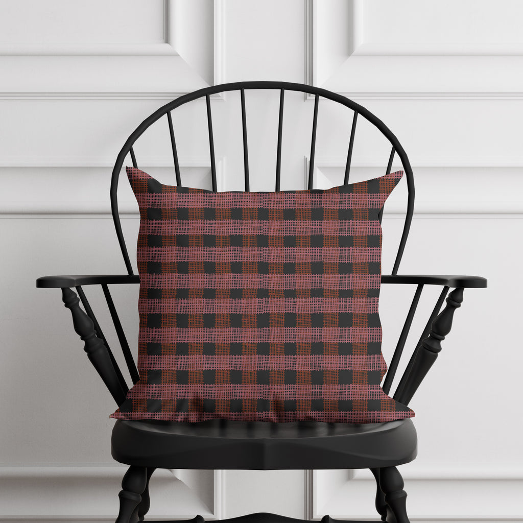 Red and black checkered pillow on a black chair against a white paneled wall.