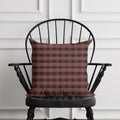 Red and black checkered pillow on a black chair against a white paneled wall.