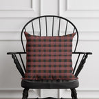 Red and black checkered pillow on a black chair against a white paneled wall.