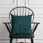 Teal patterned pillow on a black chair against a white paneled wall