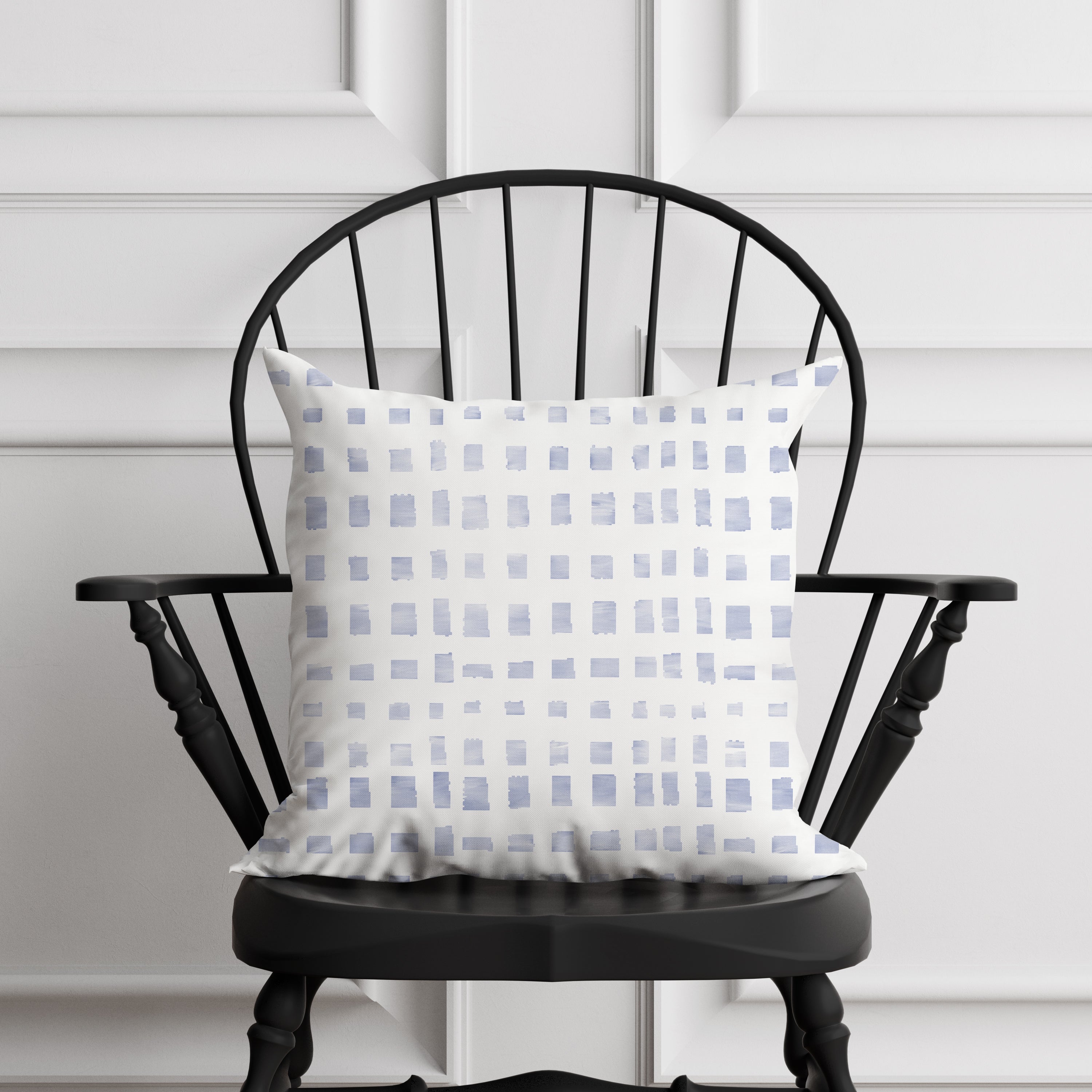 Decorative pillow with a blue and white pattern on a black chair against a white paneled wall.