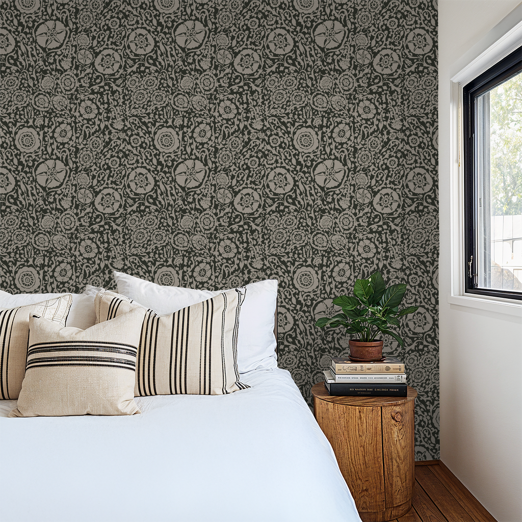 Intricate black floral wallpaper in a cozy bedroom with white bedding and wooden side table.