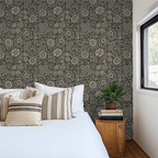Intricate black floral wallpaper in a cozy bedroom with white bedding and wooden side table.